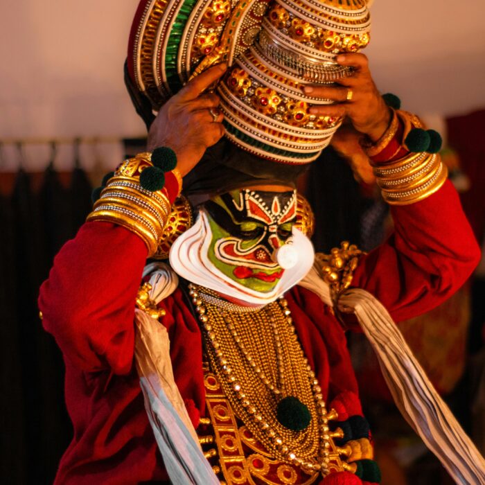 A vibrant Kathakali performer adjusts his ornate headpiece backstage, showcasing traditional Indian dance costume.