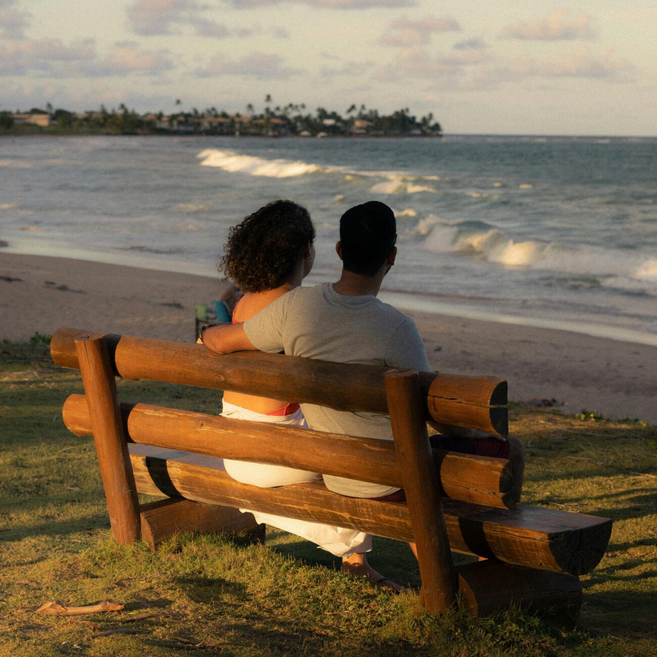 Couple embracing on a wooden bench overlooking the ocean at sunset. Perfect for romance and travel themes.